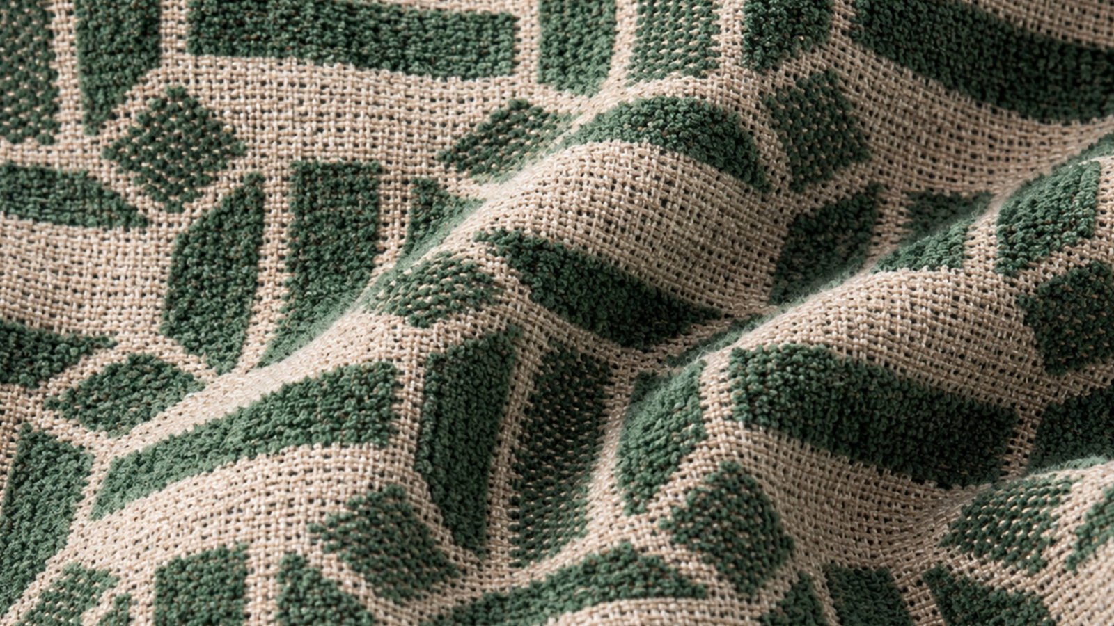 Close-up of a textured beige fabric with green geometric shapes woven in, showing raised green sections and a coarse weave.