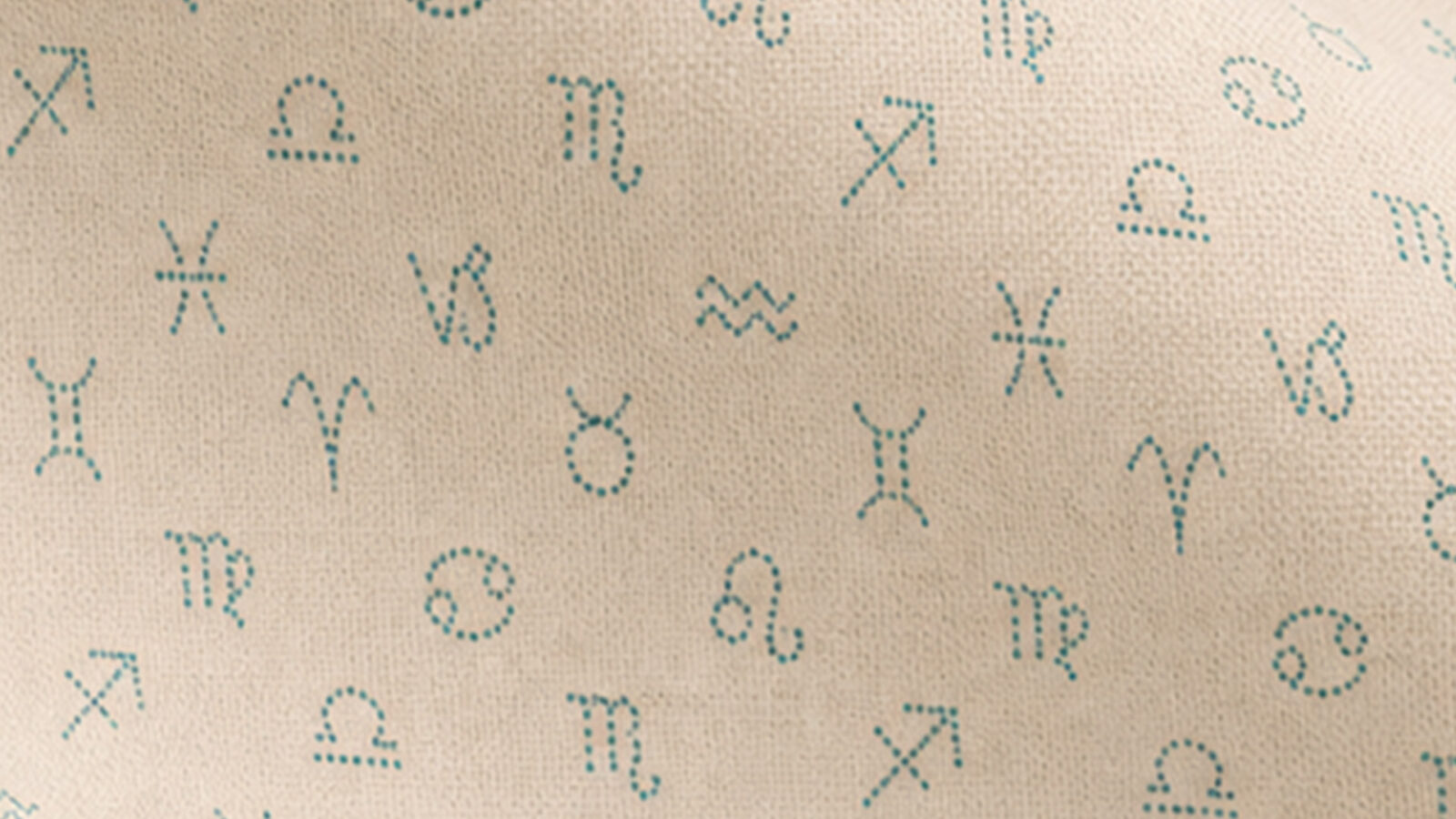 Beige fabric with teal embroidered zodiac symbols scattered across the surface.